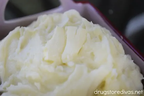 Mashed potatoes with a pat of butter on top in a maroon bowl.