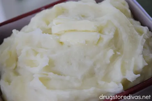 Mashed potatoes with a pat of butter on top in a maroon bowl.