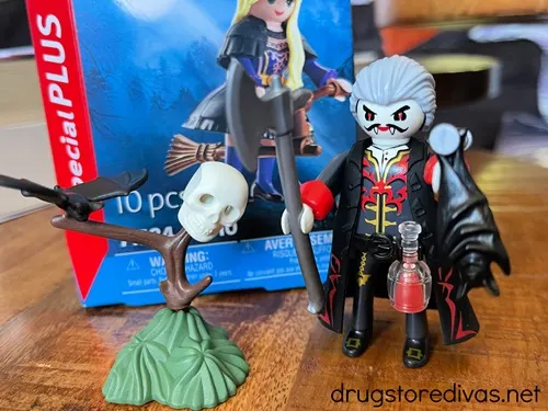 A toy vampire in next to a toy tree and a Halloween toy in a box behind them.