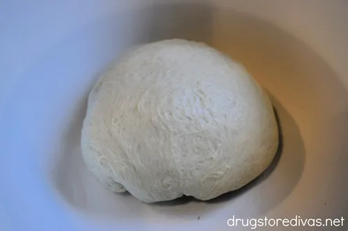 A pizza dough ball in a white bowl.