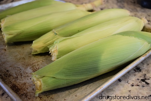 Five ears of corn in husks on a sheet pan.