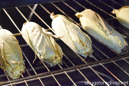 Five ears of corn on the husk on a rack in the oven.