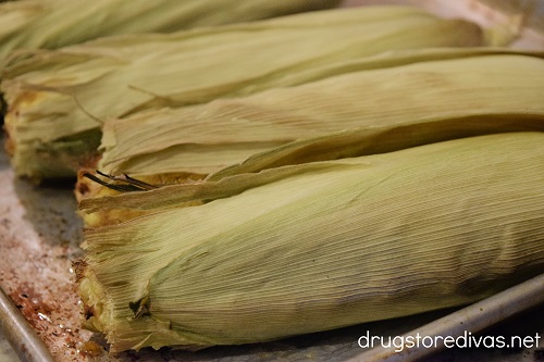 Four ears of cooked corn in husks on a sheet pan.