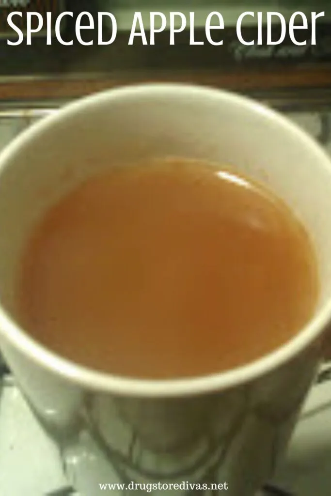 Apple cider in a white mug with the words "Spiced Apple Cider" digitally written on top.