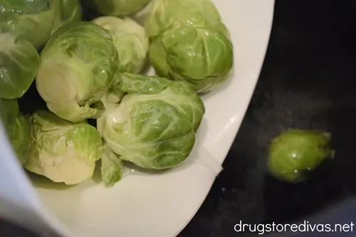 Brussel sprouts in a bowl being poured into a pot of water.