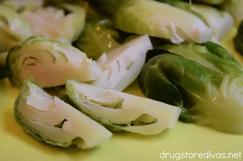 Quartered Brussels sprouts on a green cutting board.