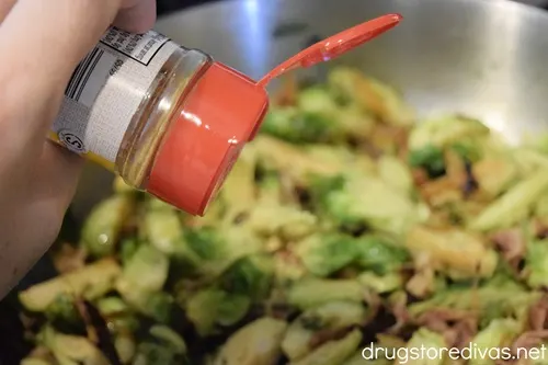 Seasoning being added to Brussels sprouts in a silver pan.