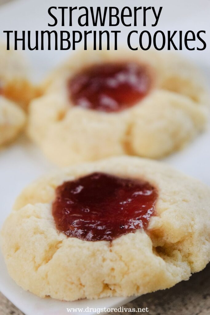 Two thumbprint cookies with red jelly in the center with the words "Strawberry Thumbprint Cookies" digitally written on top.
