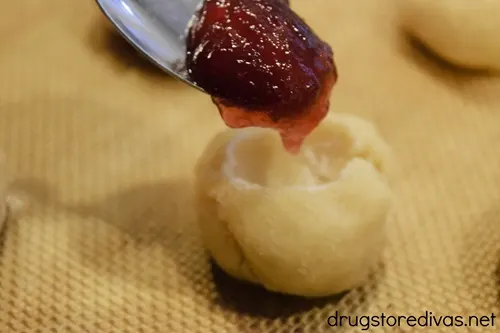 A spoon with red jelly on it over a cookie dough ball with a well in it.