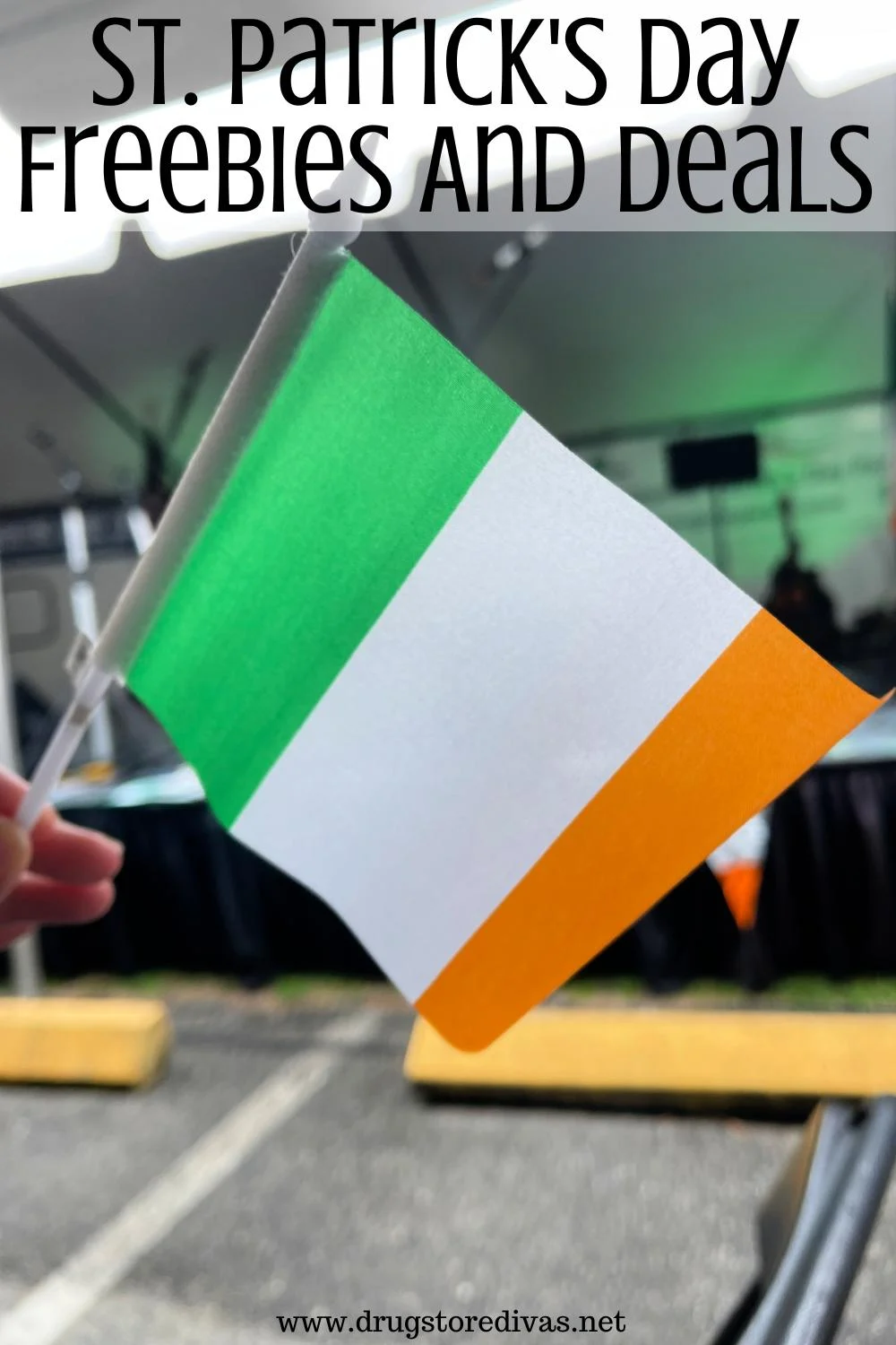 A hand holding an Irish flag in front of a stage in a parking lot with the words 