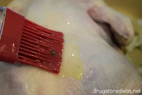 Melted butter being brushed onto a whole chicken.