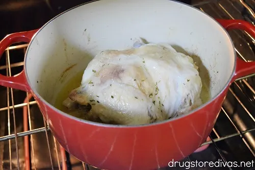 A whole chicken in a red Dutch oven in the oven.