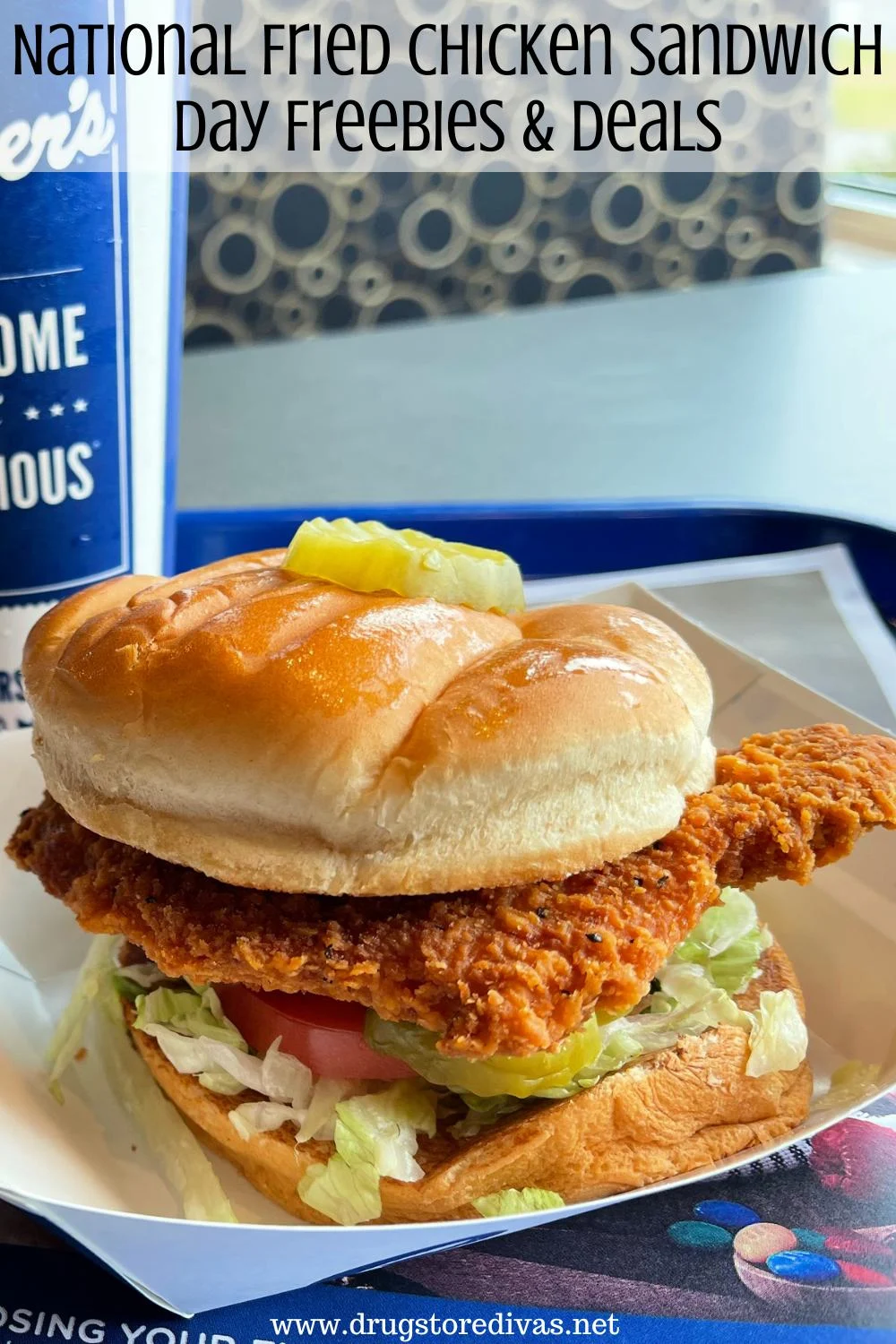 A fried chicken sandwich is a paper basket on a table with a drink behind it and the words 
