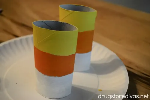 Two toilet paper roll tubes, painted yellow, orange, and white, on a paper plate.