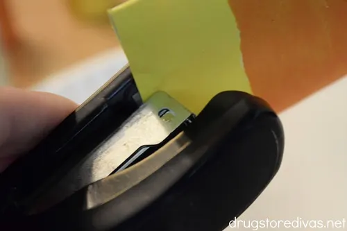 A stapler stapling a white and orange paper.