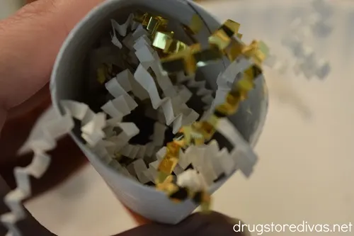 White and gold paper shred in a cardboard tube.