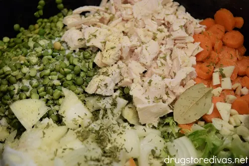 Diced chicken, split peas, sliced carrots, sliced onions, and garlic with seasoning on top in a slow cooker.
