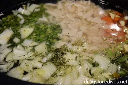 Diced chicken, split peas, sliced carrots, sliced onions, and garlic with water on top in a slow cooker.