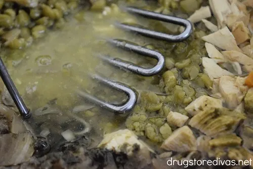 Split pea soup being mashed with a potato masher.