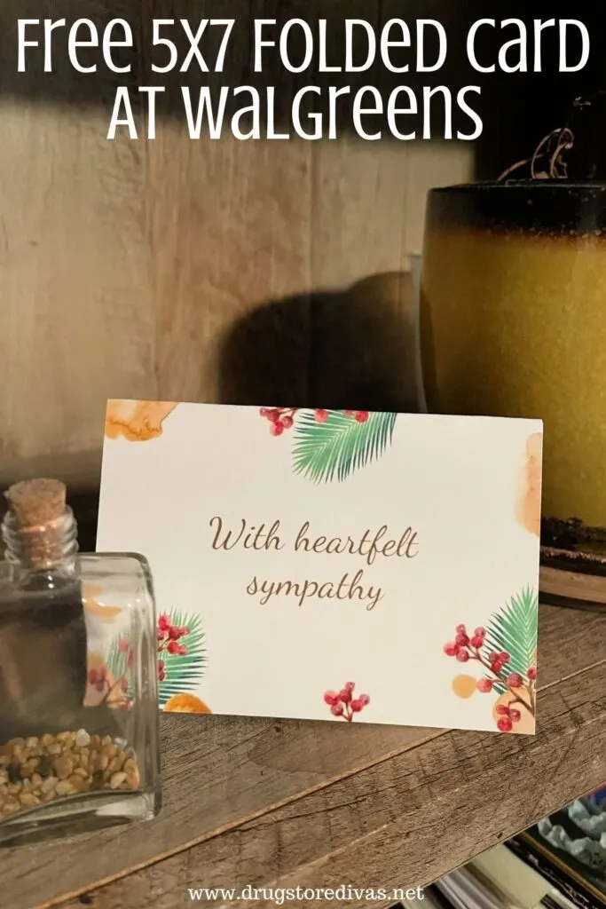 Folded card that says "With Deepest Sympathy" on a wooden shelf with a plant behind it and a jar with rocks in front of it and the words "Free 5x7 Folded Card At Walgreens" digitally written on top.