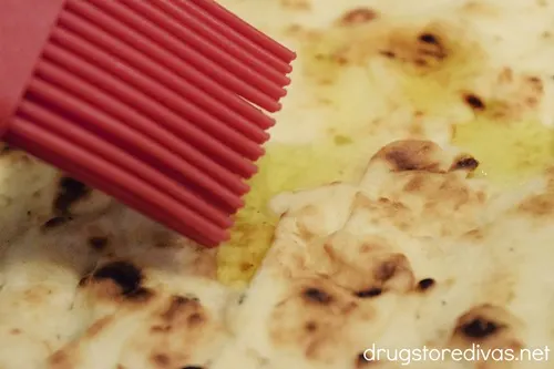 A red pastry brush brushing olive oil on naan bread.