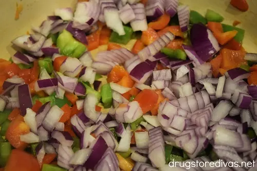 Red and green bell pepper pieces and red onion pieces in a Dutch oven.