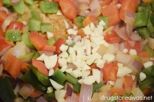 Red and green bell pepper pieces, red onion pieces, and garlic pieces in a Dutch oven.