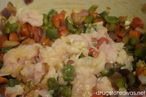 Red and green bell pepper pieces, red onion pieces, and shredded chicken in a Dutch oven.