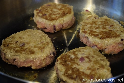 Four partially cooked turkey burger patties in a skillet on the stove top.