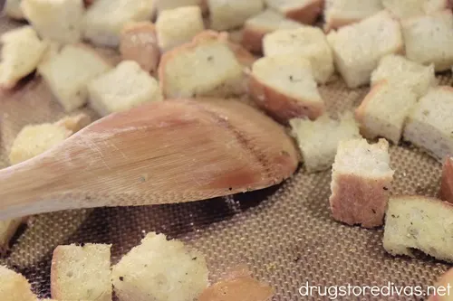 A spoon stirring bread cubes on a baking mat.