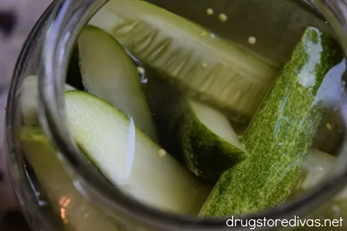 A jar of liquid filled with pickle spears.