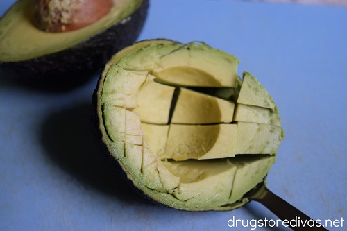 Half an avocado cut into slices in the skin and an uncut half behind it.