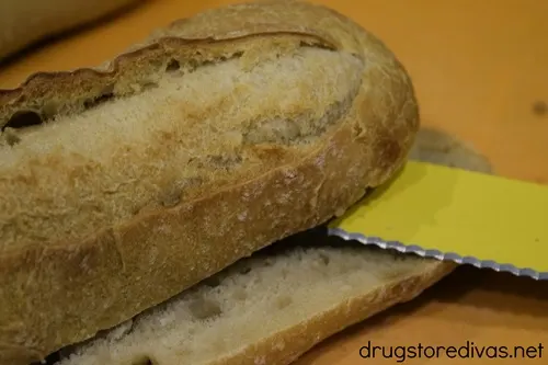 A loaf of French bread being cut in half by a yellow knife.