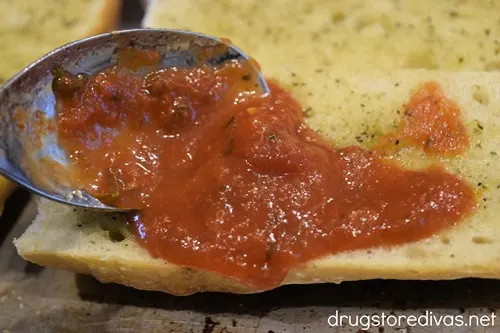 A spoon spooning pasta sauce onto French bread.
