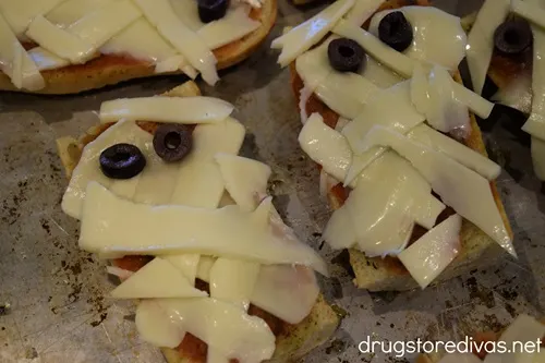 Uncooked French bread pizzas that look like a mummy on a cookie sheet.