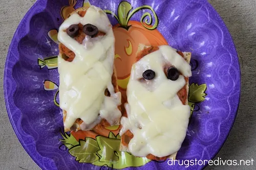 Two French bread pizzas that look like a mummy in a purple bowl.