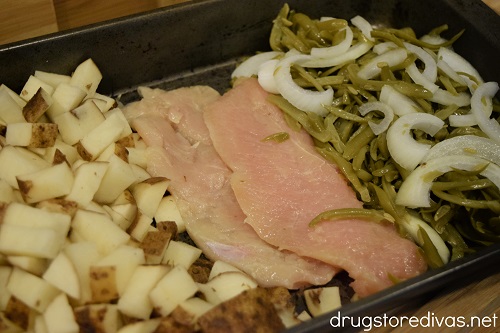 Chicken, diced potatoes, sliced onion, and green beans in a pan.
