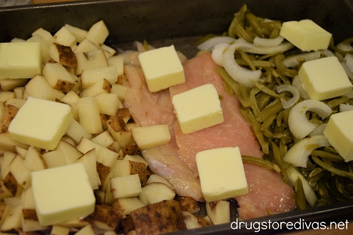 Butter, chicken, diced potatoes, sliced onion, and green beans in a pan.