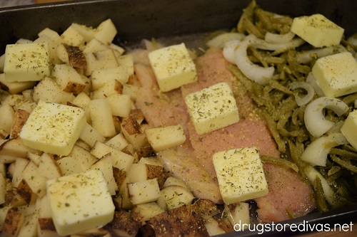 Seasoning, butter, chicken, diced potatoes, sliced onion, and green beans in a pan.