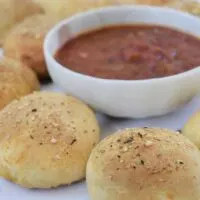 Ten rolls surrounding marinara sauce that's in a bowl with the words 