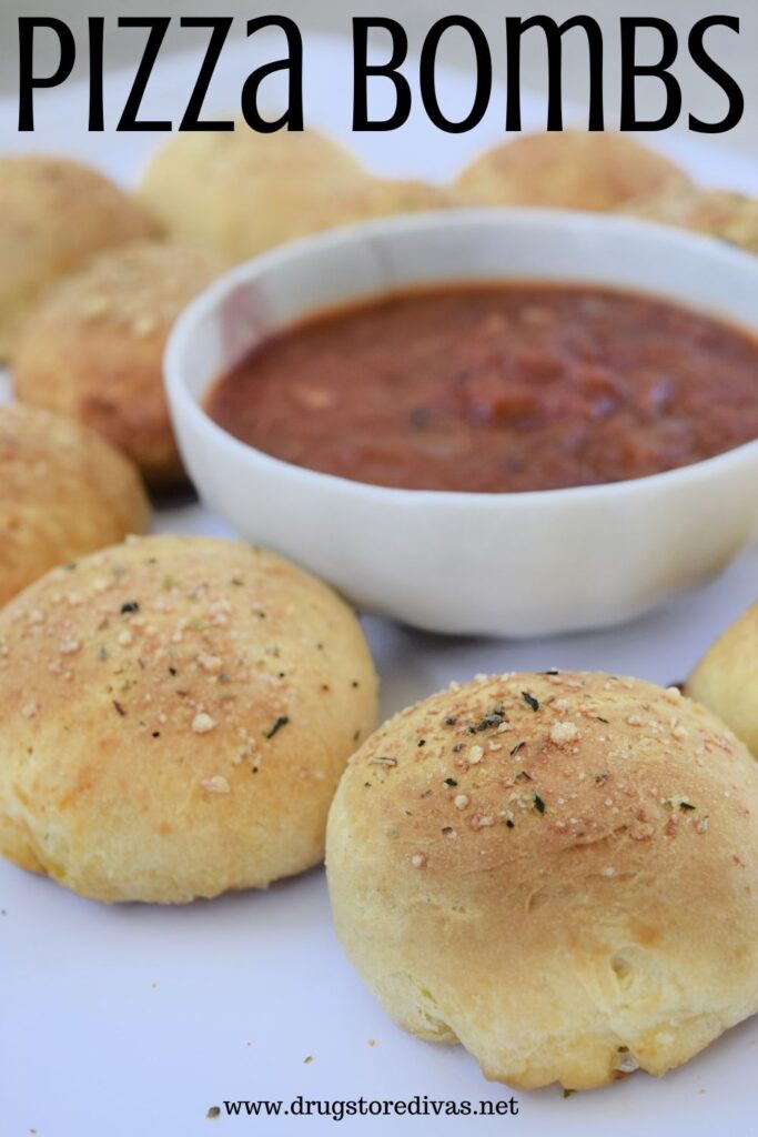 Ten rolls surrounding marinara sauce that's in a bowl with the words "Pizza Bombs" digitally written on top.