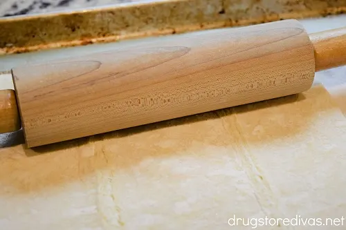 A rolling pin rolling out a puff pastry sheet.