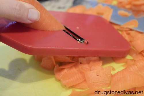 A carrot being cut on a red mandolin slicer.