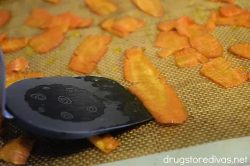 A brown spatula flipping carrot slices on a baking sheet.