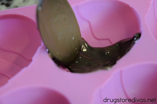 Melted chocolate being spooned into an Easter egg mold.
