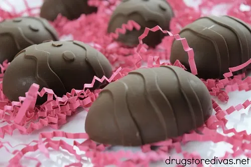 Six homemade peanut butter eggs on pink paper shred.