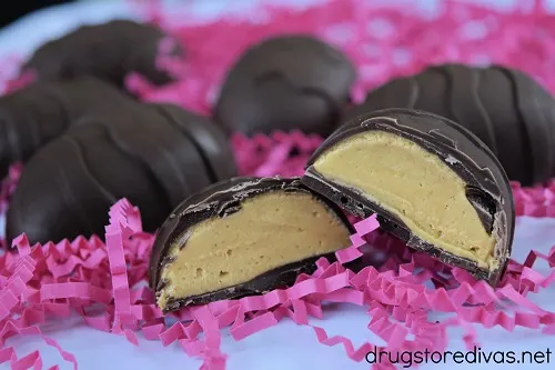Five peanut butter eggs on pink paper shred, with one cut in half.