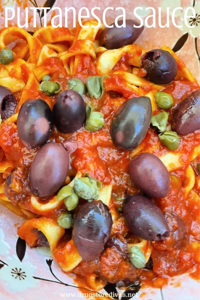 A bowl of pasta with a red tomato sauce with olives and capers with the words "Puttanesca Sauce" digitally written on top.