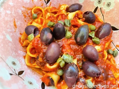 A bowl of pasta with a red tomato sauce with olives and capers.
