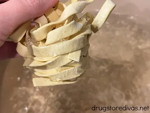 A hand dropping fresh fettuccini into a pot of boiling water.